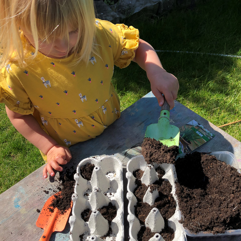 A young child scooping soil into an egg carton