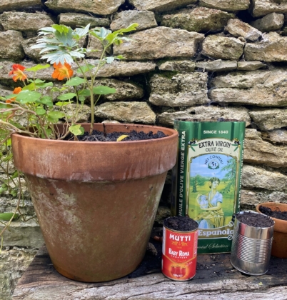 A plant pot with flowers next to 3 recycled planter cans